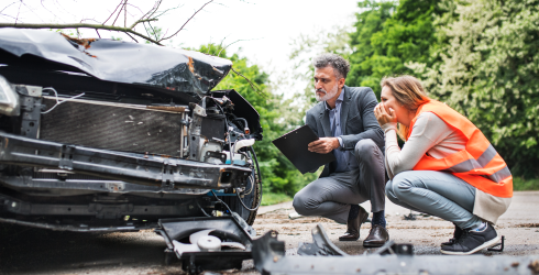Ein Gutachter inspiziert mit einer Frau ein Auto nach einem Unfall