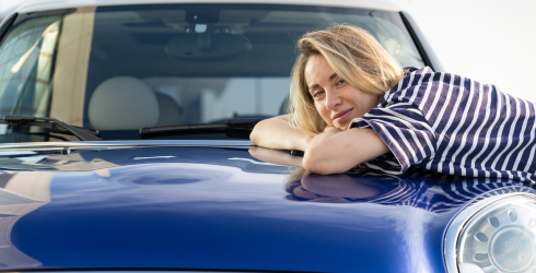 Frau lehnt auf der Motorhaube eines blauen Autos