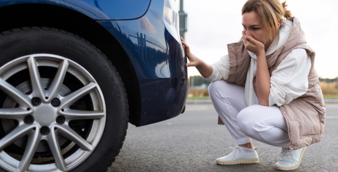 Frau untersucht Schaden an der Heckstoßstange von einem blauen Auto