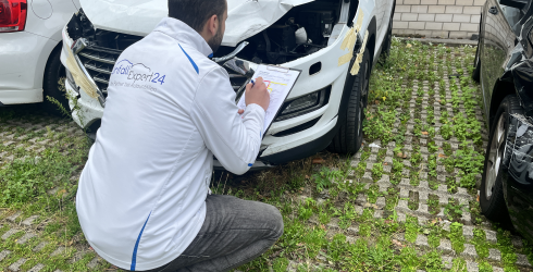 Ein Unfallgutachter von UnfallExpert24 kniet vor einem beschädigten Auto und erstellt ein Guthaben. 
