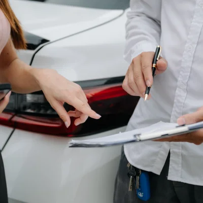 Ein Mann und eine Frau stehen vor einem weißen Auto mit einem Klemmbrett in der Hand