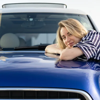 Frau lehnt auf der Motorhaube eines blauen Autos