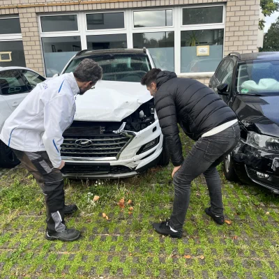 Ein Unfallgutachter von UnfallExpert24 begutachtet mit einem anderen Mann ein beschädigtes Auto 