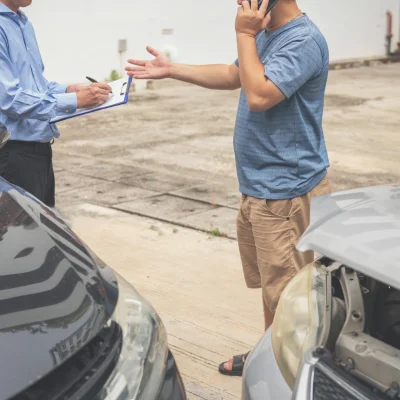 Versicherungsbeamter und ein Mann stehen vor zwei Autos die einen Unfall hatten