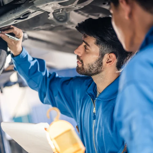 Zwei KFZ Mechaniker überprüfen den Unterboden eines Fahrzeugs
