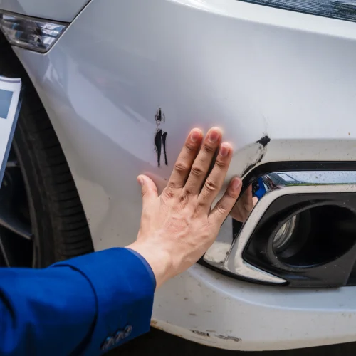 Ein Mann beurteilt einen Fahrzeugschaden an einem weißen Auto mit Lackschäden