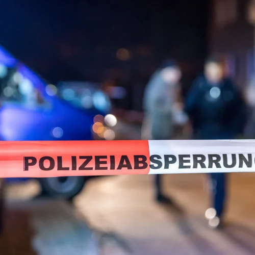 Der Tatort befindet sich in einer Stadtstraße, im Vordergrund ist ein weißes und rotes Polizeiband gespannt