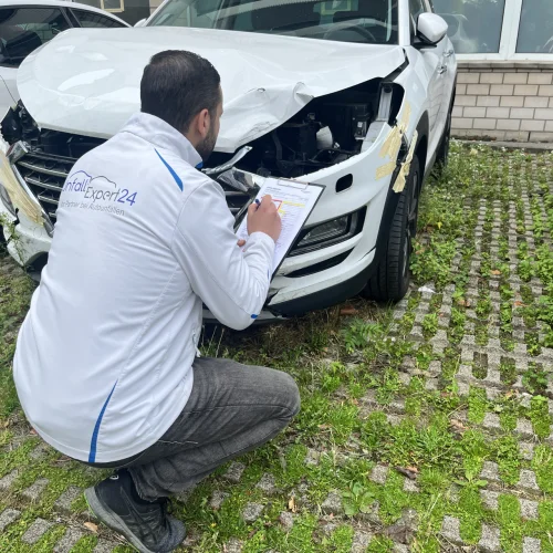 Ein Unfallgutachter von UnfallExpert24 kniet vor einem beschädigten Auto und erstellt ein Guthaben. 