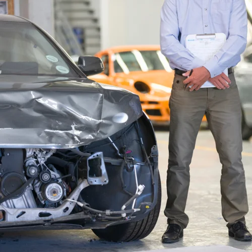 Versicherungsgutachter, der neben einem beschädigten Fahrzeug mit Unterlagen steht.