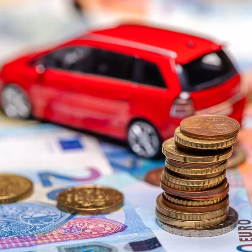 Turm mit Euro-Münzen auf dem Hintergrund von Banknoten und rotem Spielzeugauto